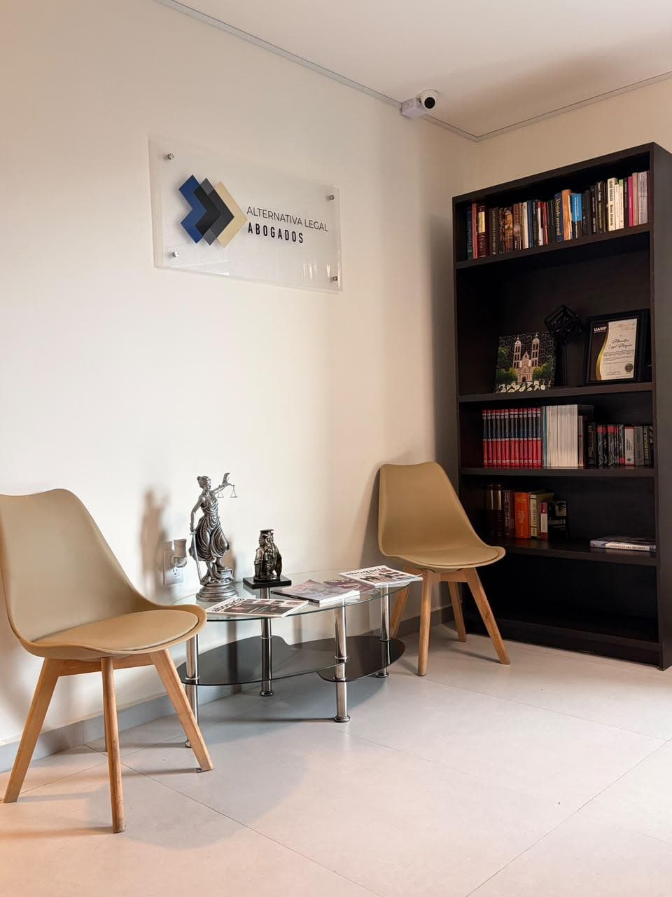 Sala de espera del despacho, con librero y la placa de la marca en la pared.